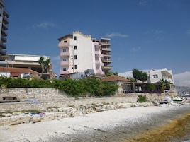 Un edificio sul lungomare con balconi, un muro in pietra e una spiaggia in primo piano.