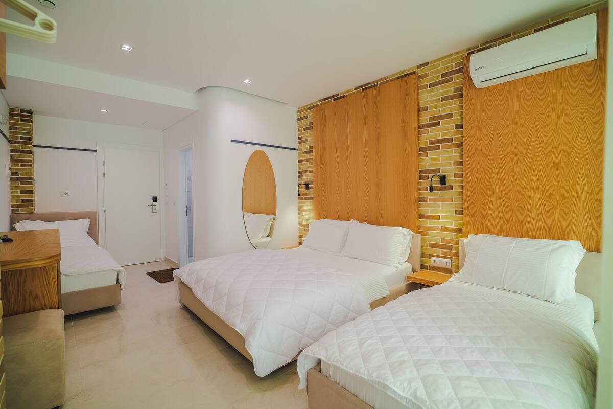 A hotel room with two beds, a wooden headboard, a brick accent wall, and an air conditioning unit.