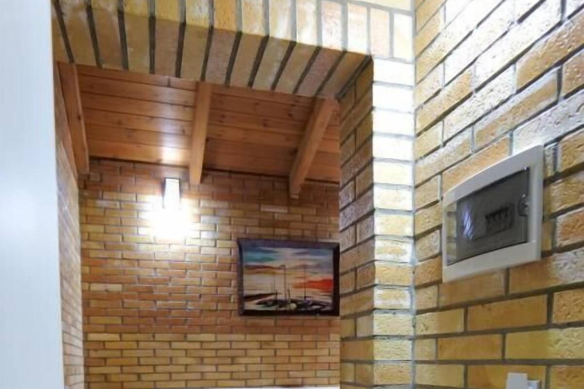 A hotel room with a brick wall, a bed with white linens, a nightstand, a wall-mounted TV, and a door with a handle.