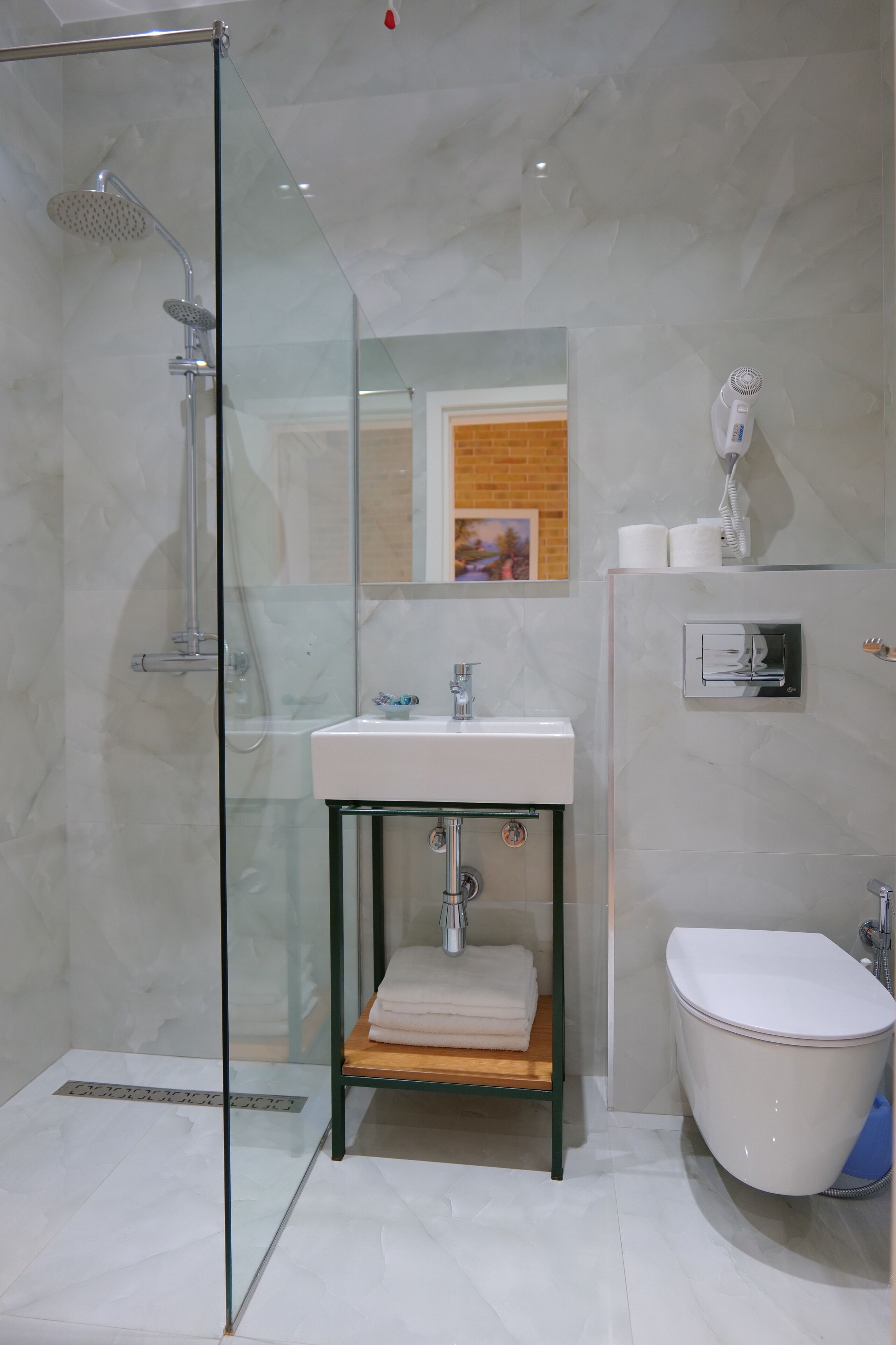 A modern bathroom with a glass-enclosed shower, a sink with a wooden shelf, a toilet, and a wall-mounted hairdryer.