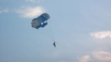 A person skydiving with a parachute against a clear sky.