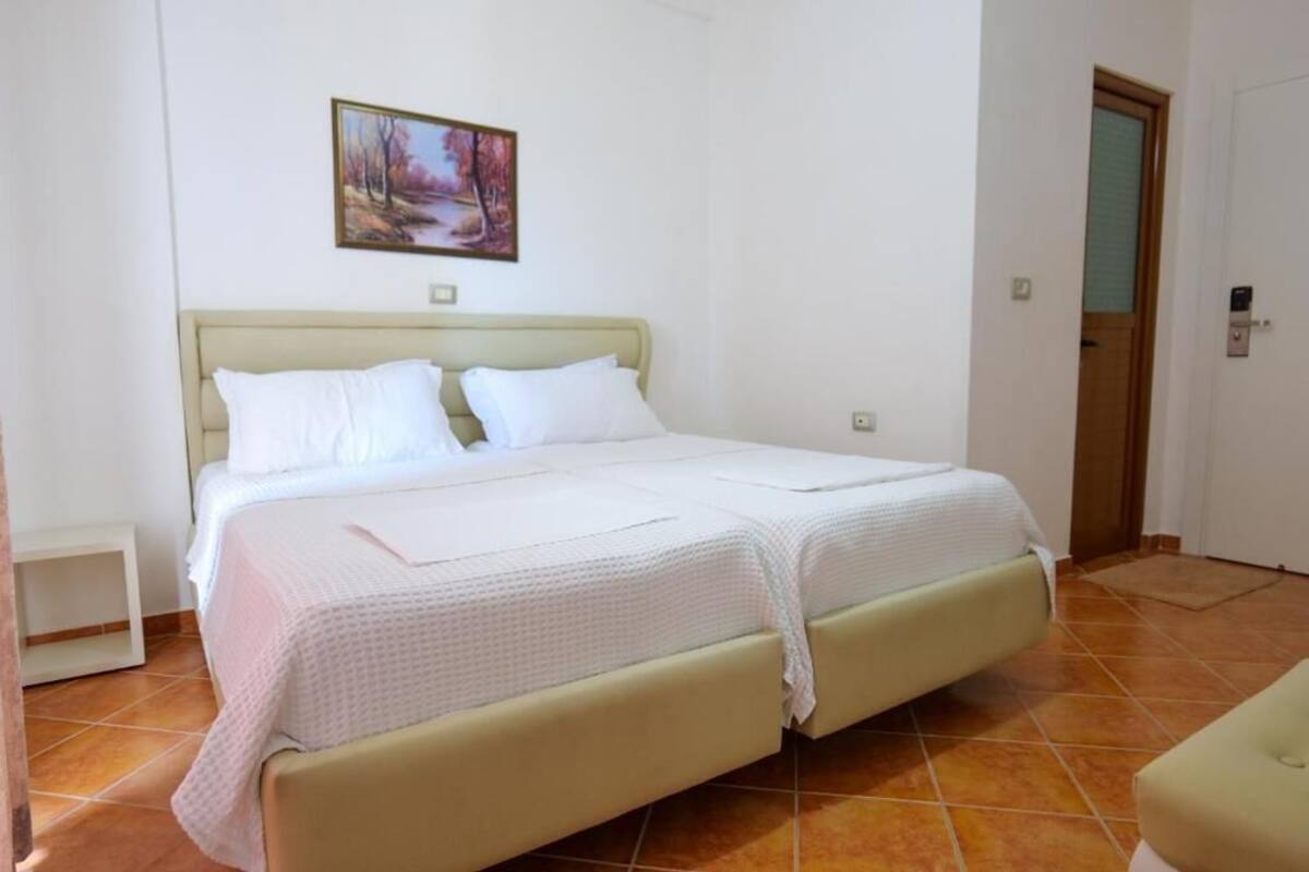 A bedroom with a bed, a nightstand, a door, and a wall-mounted picture.