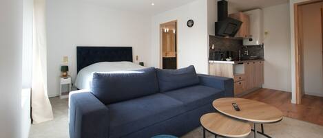 A modern living room with a sofa, ottomans, a round coffee table, and a kitchen area in the background.