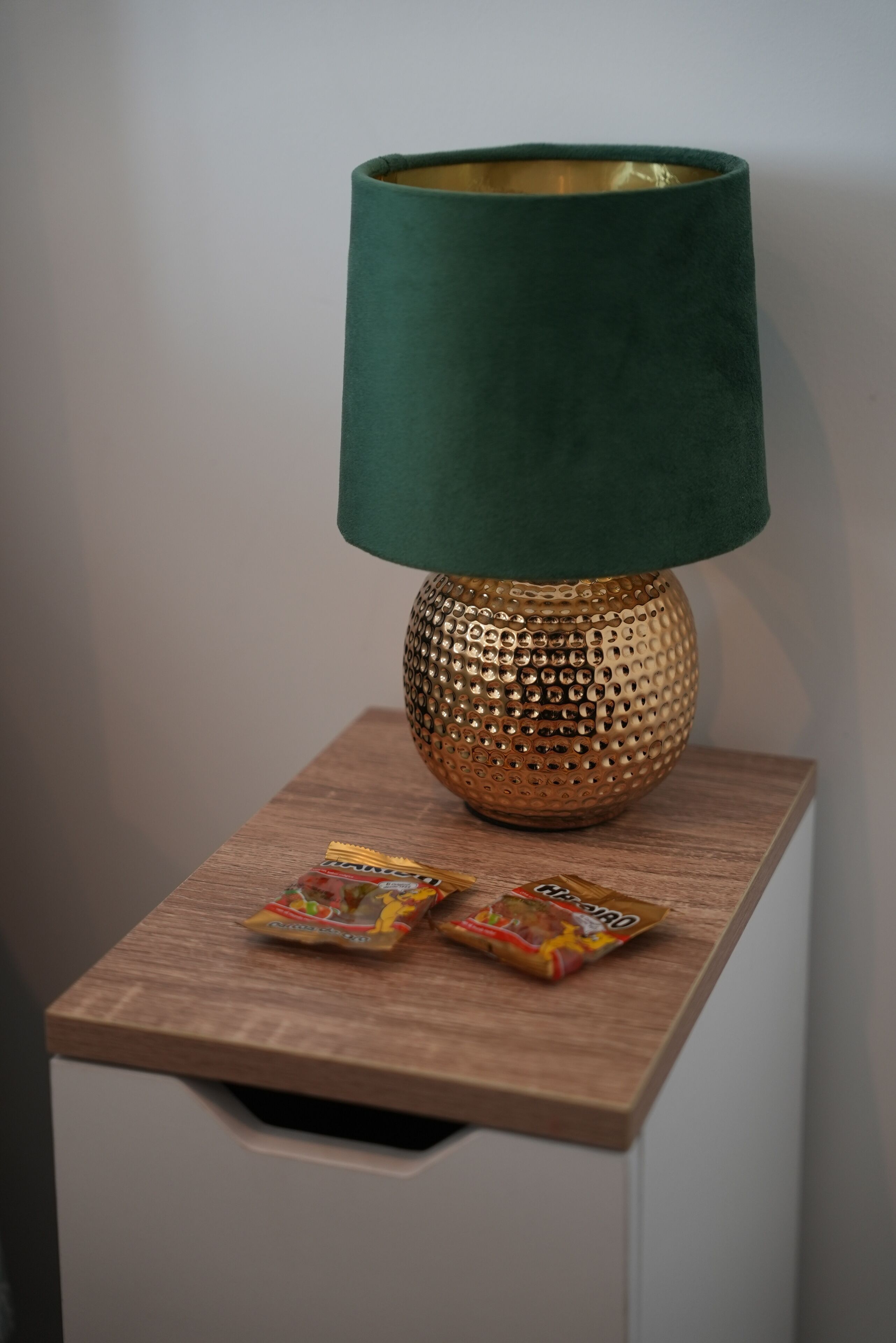 A lamp with a green shade on a wooden nightstand.