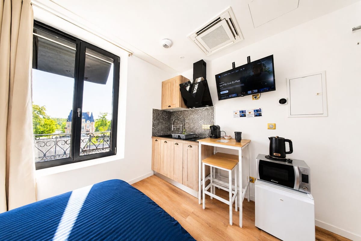 A compact room with a bed, kitchenette, and a TV.