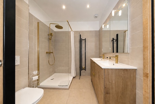 Un baño moderno con ducha de vidrio, tocador con espejo y retrete.