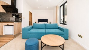 A modern living room with a blue sofa, a round wooden table, and a kitchen area with a microwave and a small fridge. - HDG Appart's Hotel Gare de L'Isle Adam (Parmain)