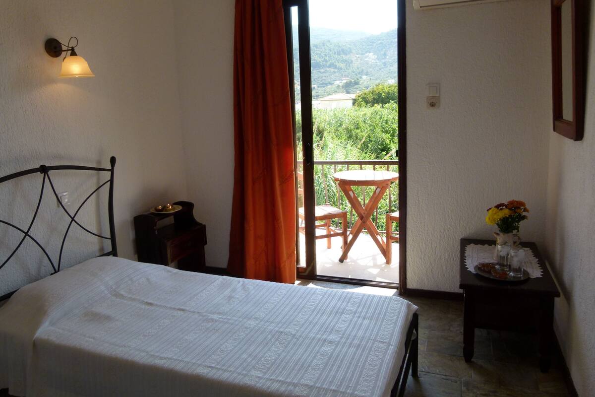 A bedroom with a bed, a small table with a vase of flowers, and a balcony with a table and chairs.