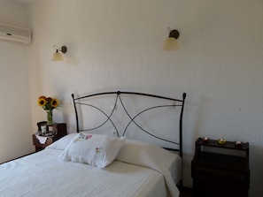 Una cama bien hecha con un cojín floral, un florero con girasoles y una mesita de noche con una lámpara y velas.