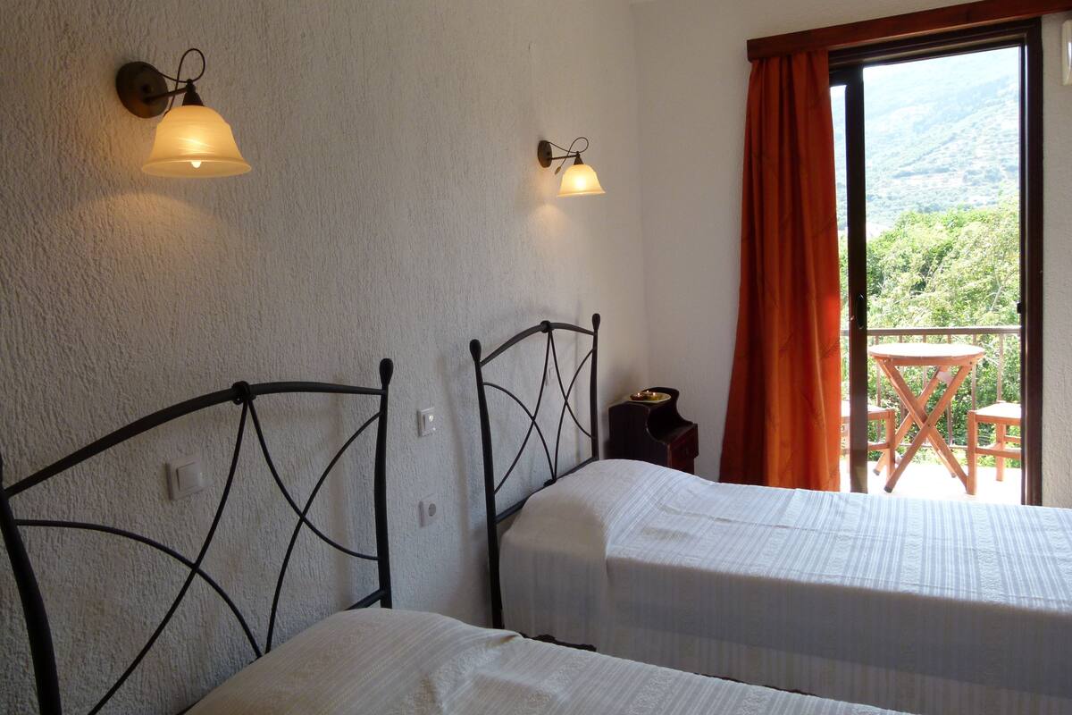 A bedroom with two beds, a small table, and a view of the outdoors.