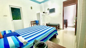 A bedroom with a bed, a desk, a chair, a television, and a door. - Tamara Motels (Hikkaduwa)
