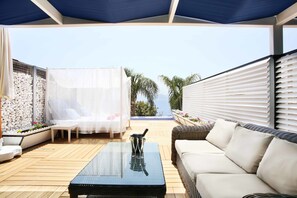 A covered outdoor seating area with a glass table, white cushioned chairs, and a wicker sofa. - Nur Beach Hotel (Kas)