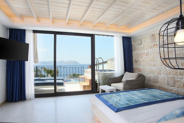 A bedroom with a bed, a TV, a balcony with a view of the sea, and a stone wall.