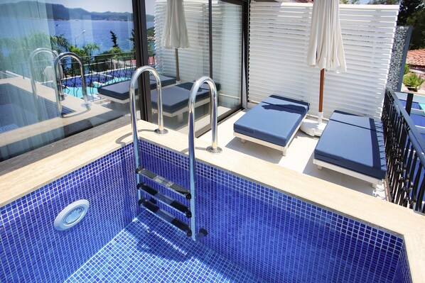 A modern indoor swimming pool with blue tiles, a glass-enclosed area, and lounge chairs. - Nur Beach Hotel (Kas)