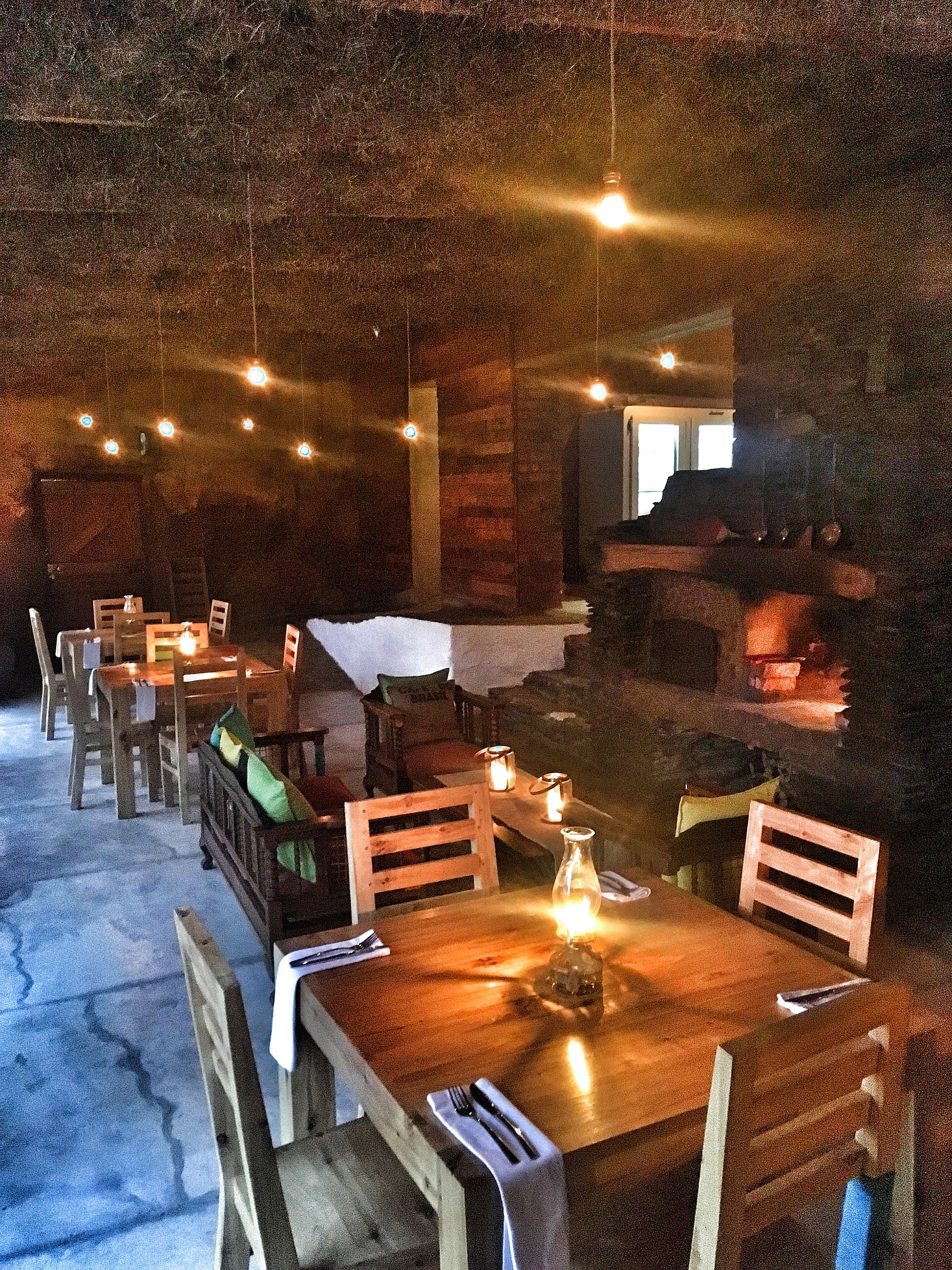 Un coin repas rustique avec des tables et des chaises en bois, des ampoules suspendues et des bougies.