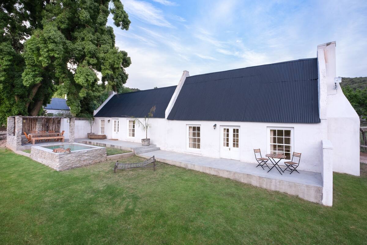 Een wit huis met een donker dak, een stenen terras en een zwembad.