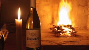 A bottle of De Krombys wine and a lit candle on a wooden table in front of a fireplace.