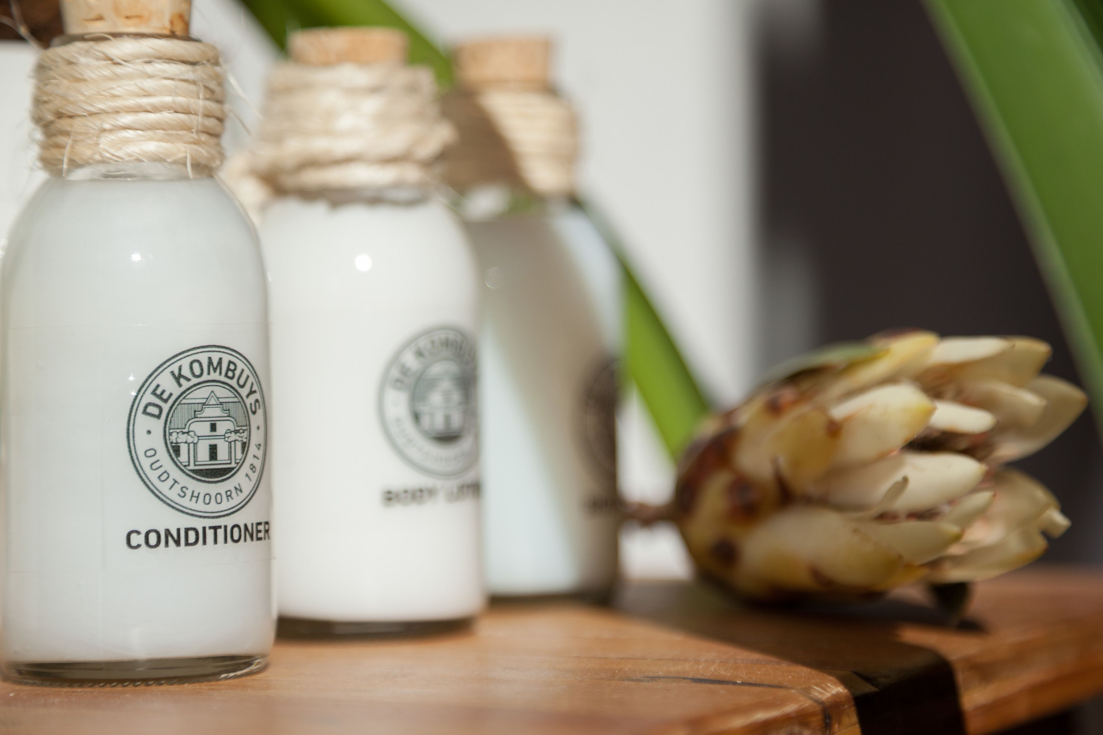 Three white bottles with labels, one of which reads "DE KOMBUYS CONDITIONER".