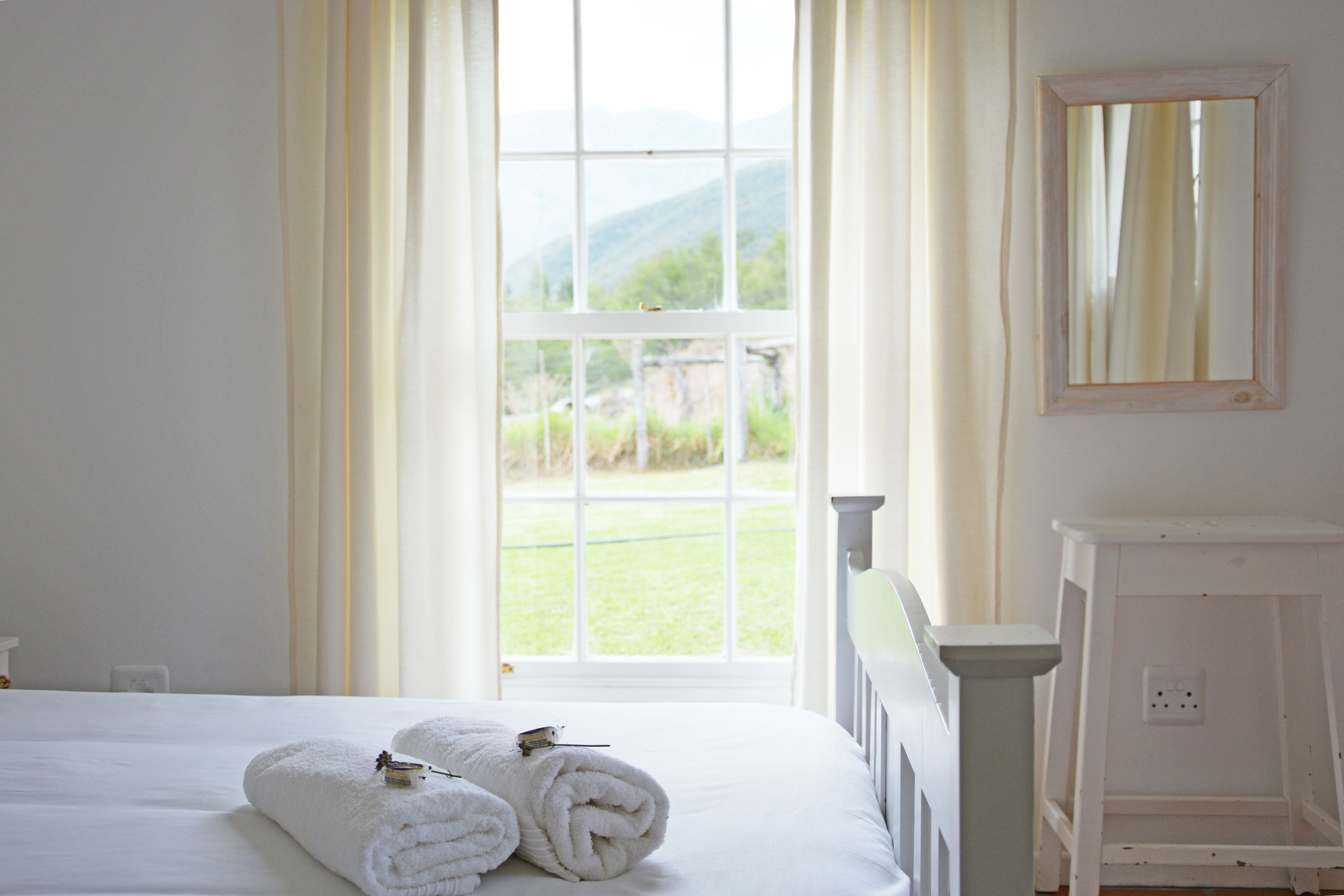 A hotel room with a bed, a window with curtains, a white dresser, and a mirror on the wall.