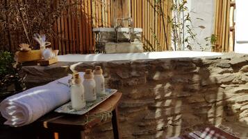 A stone-walled spa area with a hot tub, a bamboo fence, and three bottles of shampoo on a tray.