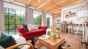 Een moderne woonkamer met een rode bank, een houten salontafel en grote ramen met uitzicht op groen.