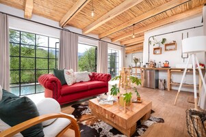 A modern living room with a red sofa, wooden coffee table, and large windows offering a view of greenery.