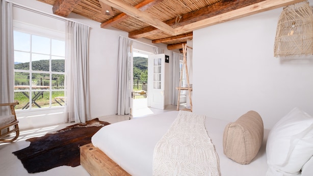 Een slaapkamer met een groot bed, houten balken, uitzicht op het omliggende landschap en een rustieke inrichting.