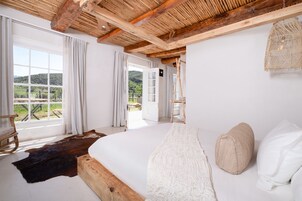 A bedroom with a large bed, wooden beams, a view of the outdoors, and a rustic decor style.