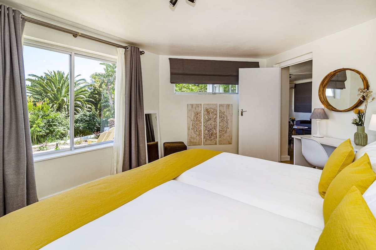 A hotel room with a bed, a desk, and a chair. There is a window with curtains, a door, and a mirror on the wall.