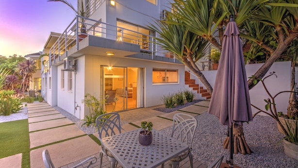 A modern two-story house with a balcony, a patio with outdoor furniture, and a variety of plants. -  Morgen Guest House (Cape Town)