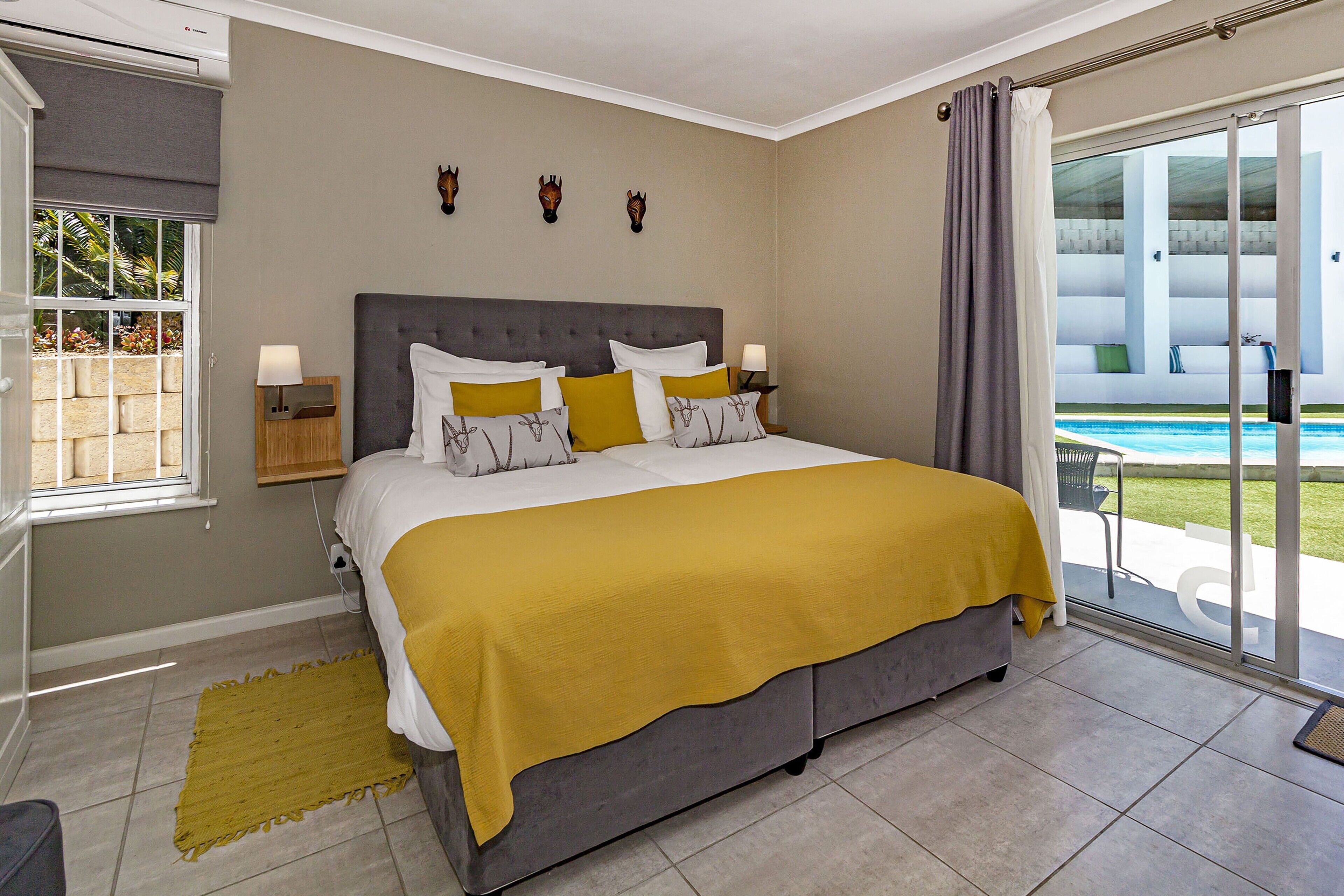 A bedroom with a bed, a window, a nightstand, and a view of a pool.