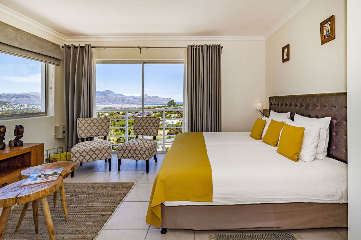 A hotel room with a large bed, a desk, a chair, and a view of the mountains.