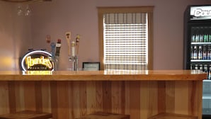 A bar area with wooden stools, a neon sign, and a refrigerator stocked with beverages.