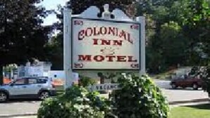 A sign for the Colonial Inn Motel with a clear view of the motel's name and a small bush in front.