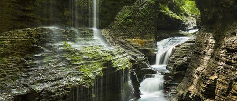 A waterfall cascading over moss-covered rocks with a wooden bridge.