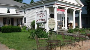A Colonial Inn & Motel with a porch, outdoor seating, and signs advertising Colonial Creamery and pottery.