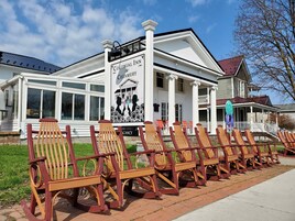 A Colonial Inn & Creamery with a white exterior, large windows, and a porch with wooden chairs.