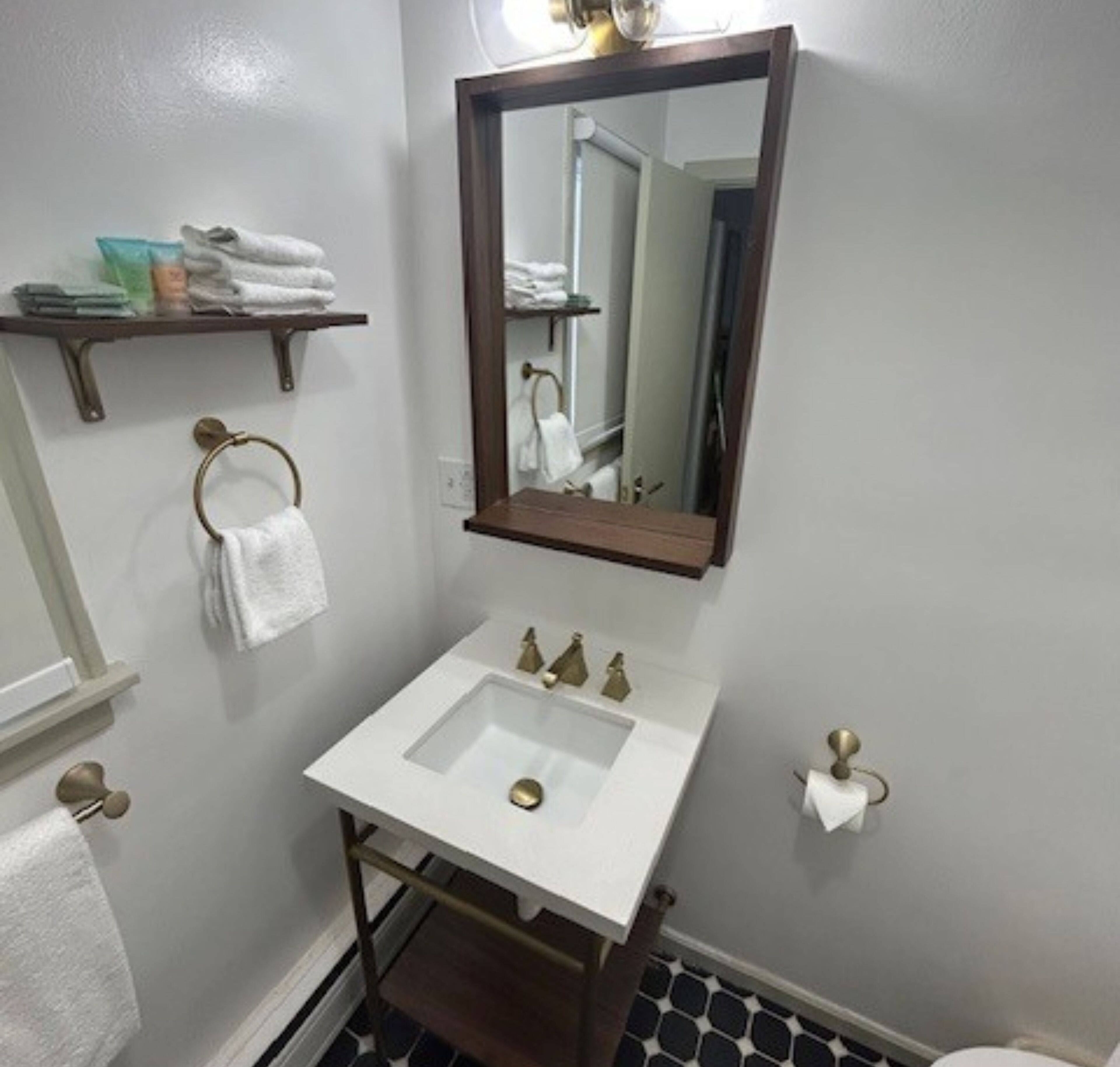 Un baño con lavamanos blanco, espejo y toallero.