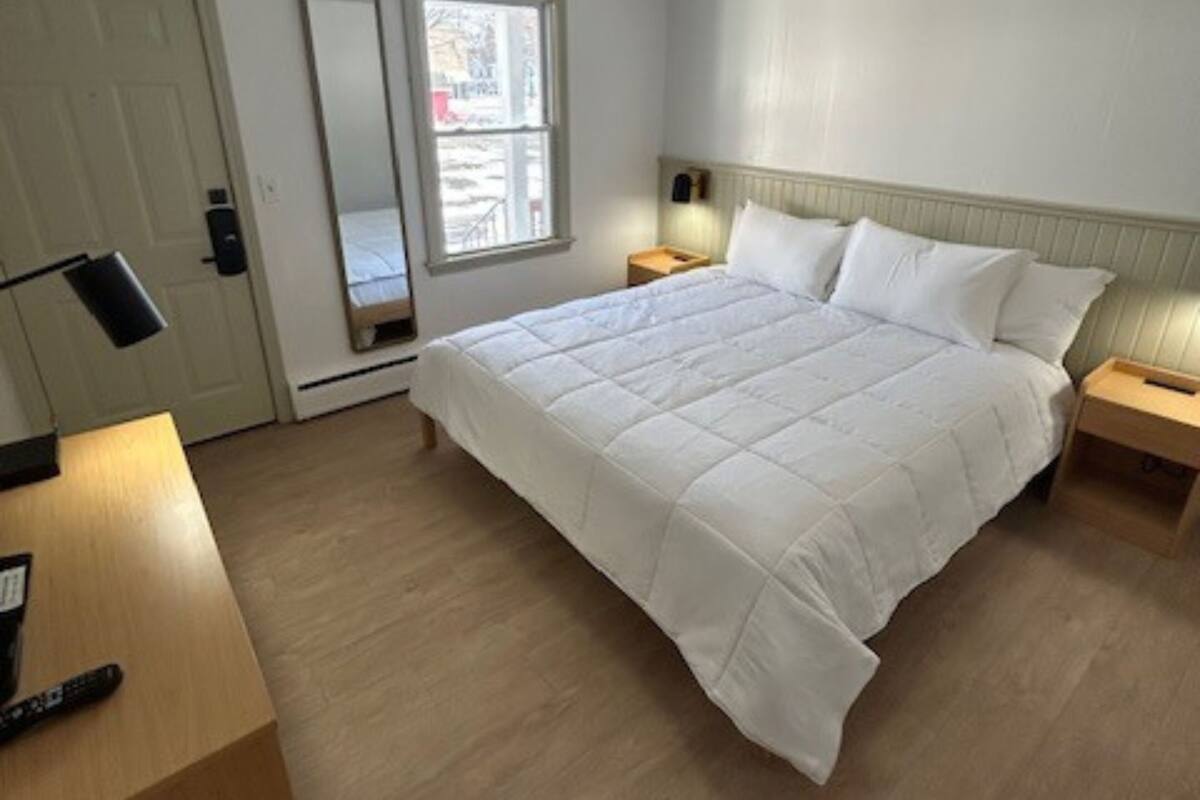 A bedroom with a large bed, bedside tables, a mirror, a door, and a window.