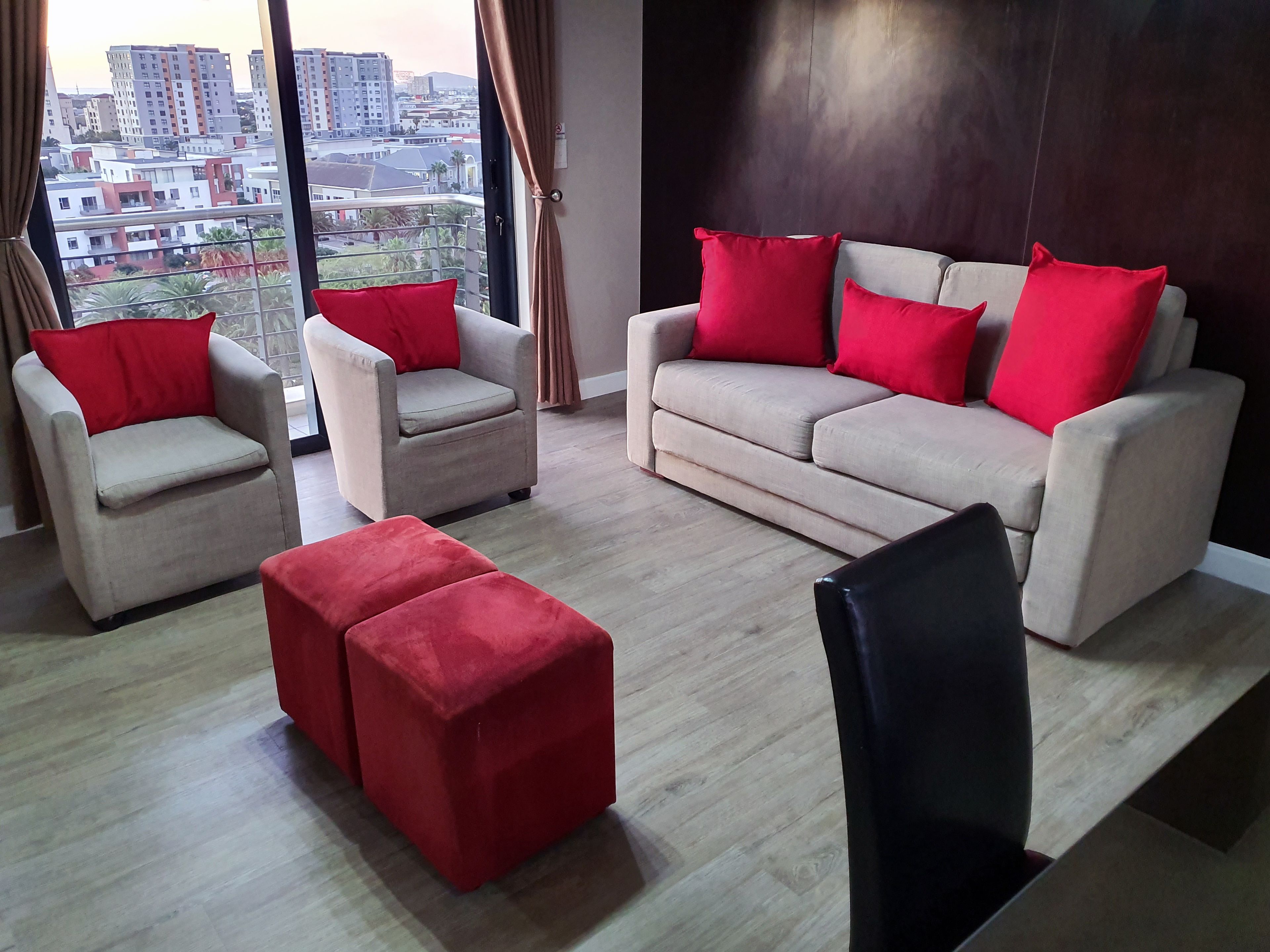 A modern living room with a sofa, two armchairs, and a red ottoman.