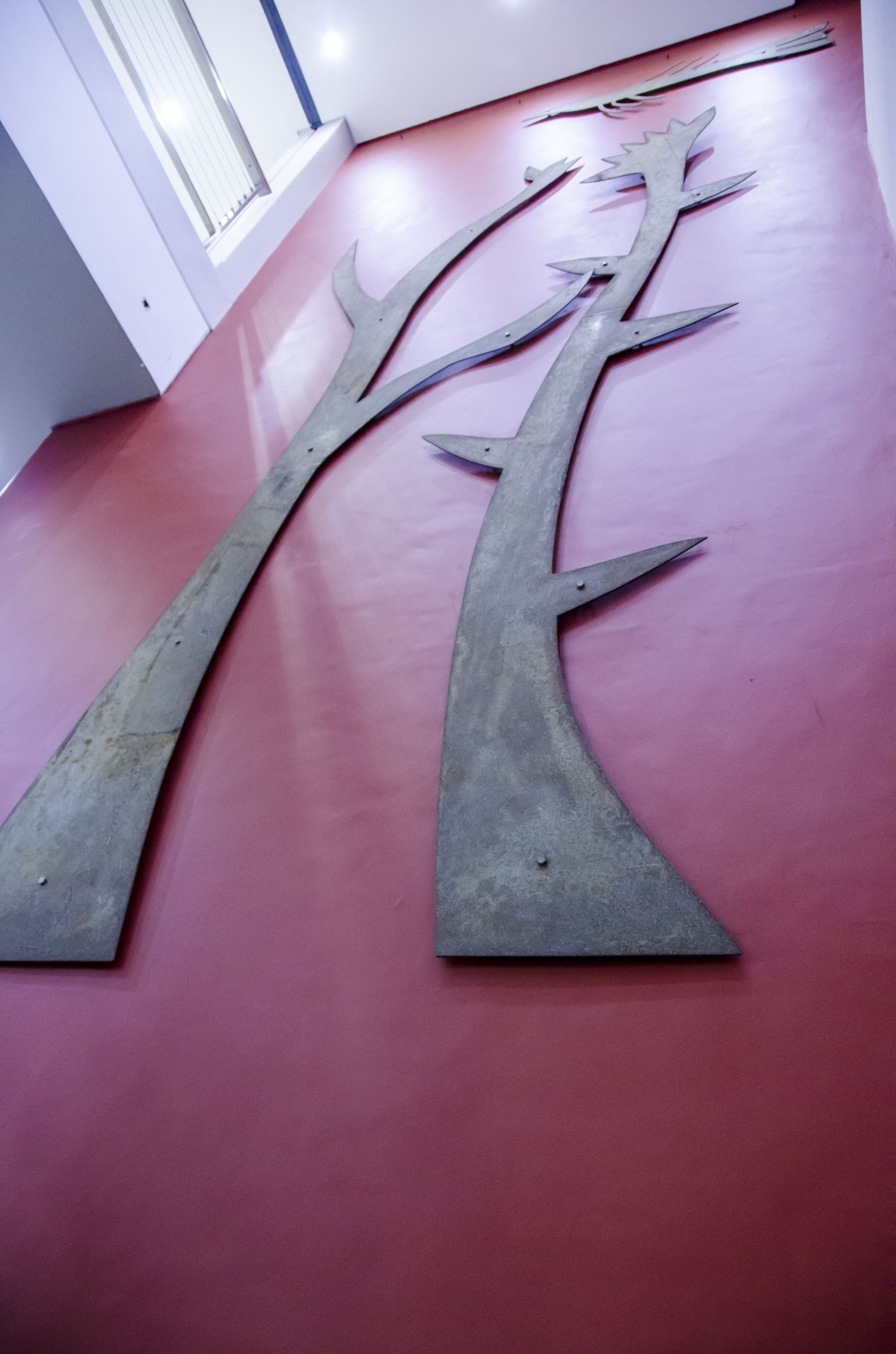 Una escultura de árbol metálico sobre un suelo rojo.