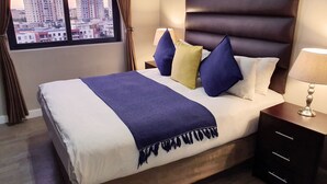 Een hotelkamer met een groot bed, een hoofdeinde, twee nachtkastjes, een lamp en uitzicht op gebouwen.