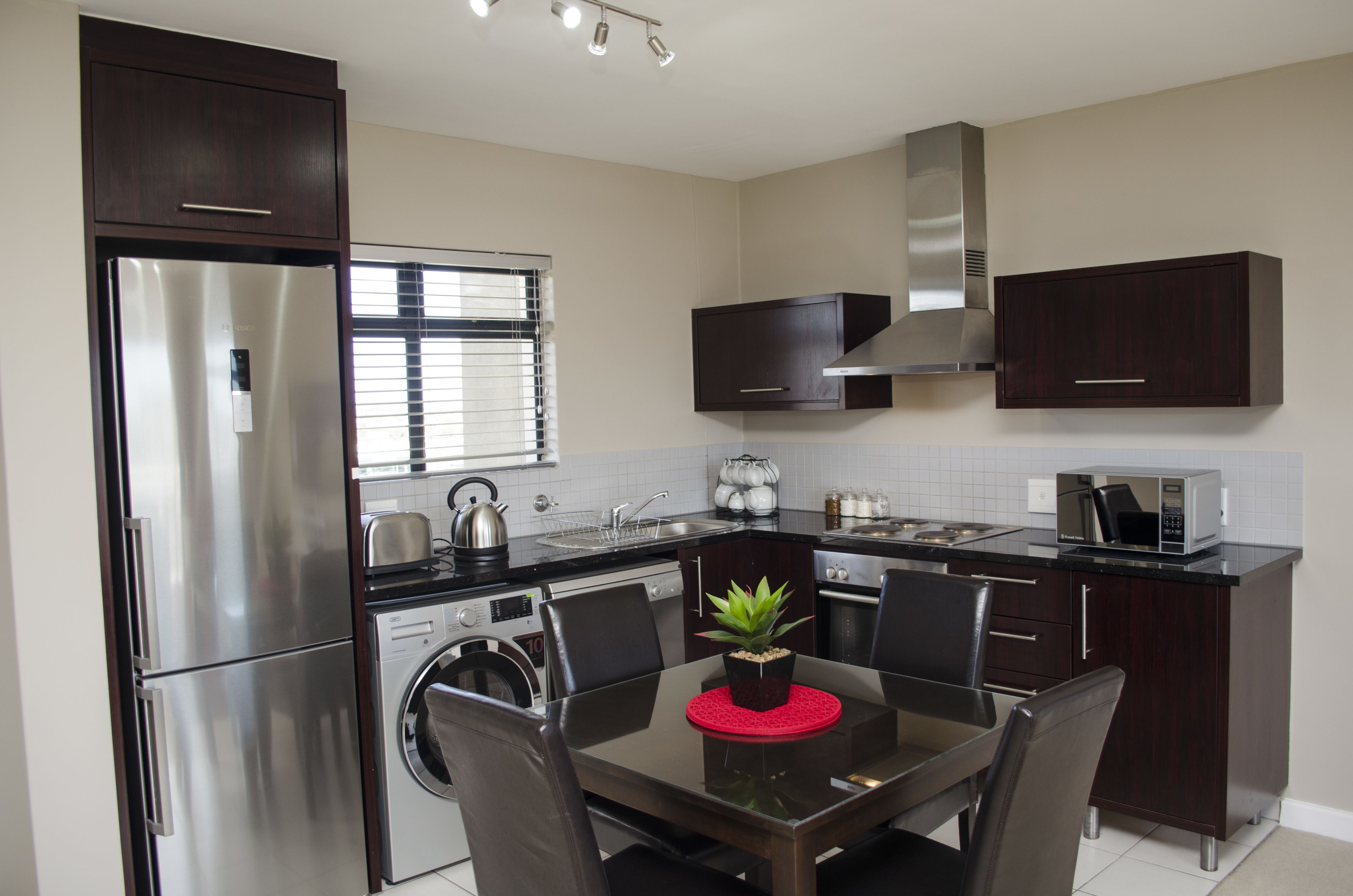 Een moderne keuken met roestvrijstalen apparatuur, donkerhouten kasten, een eettafel met stoelen en een kleine potplant.