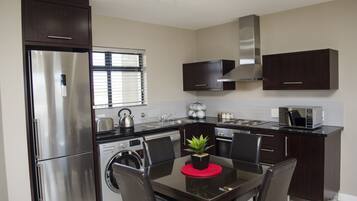 A modern kitchen with stainless steel appliances, dark wood cabinets, a dining table with chairs, and a small potted plant.