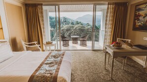 Une chambre d’hôtel avec un grand lit, un bureau et un balcon agrémenté de fauteuils en osier.