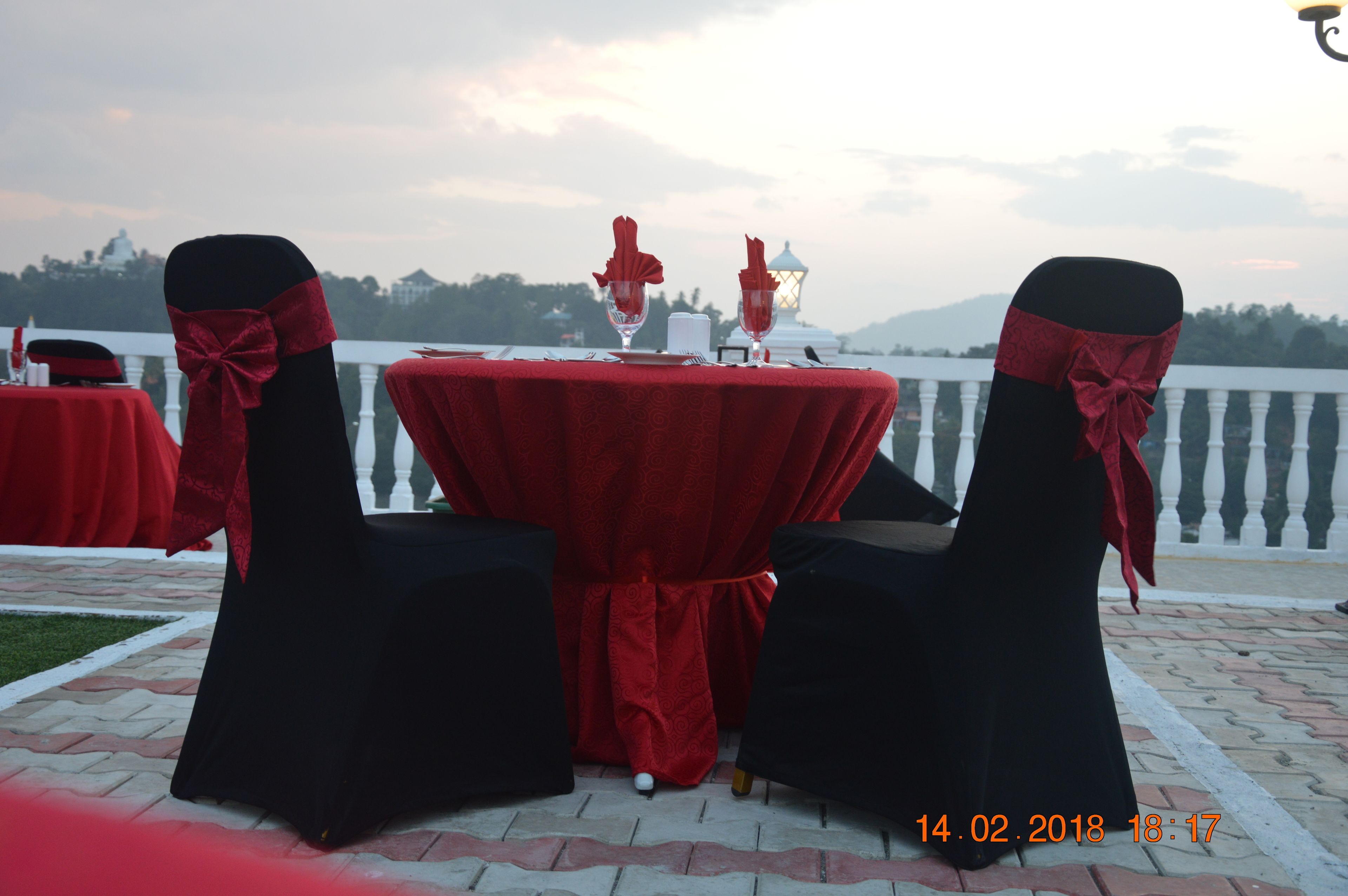 Mesa dispuesta para dos con manteles rojos y sillas negras adornadas con cintas rojas, con vistas a un paisaje pintoresco.