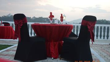 Mesa dispuesta para dos con manteles rojos y sillas negras adornadas con cintas rojas, con vistas a un paisaje pintoresco.