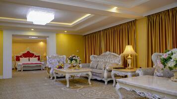 A luxurious hotel room with ornate furniture, a chandelier, and a large window with curtains.