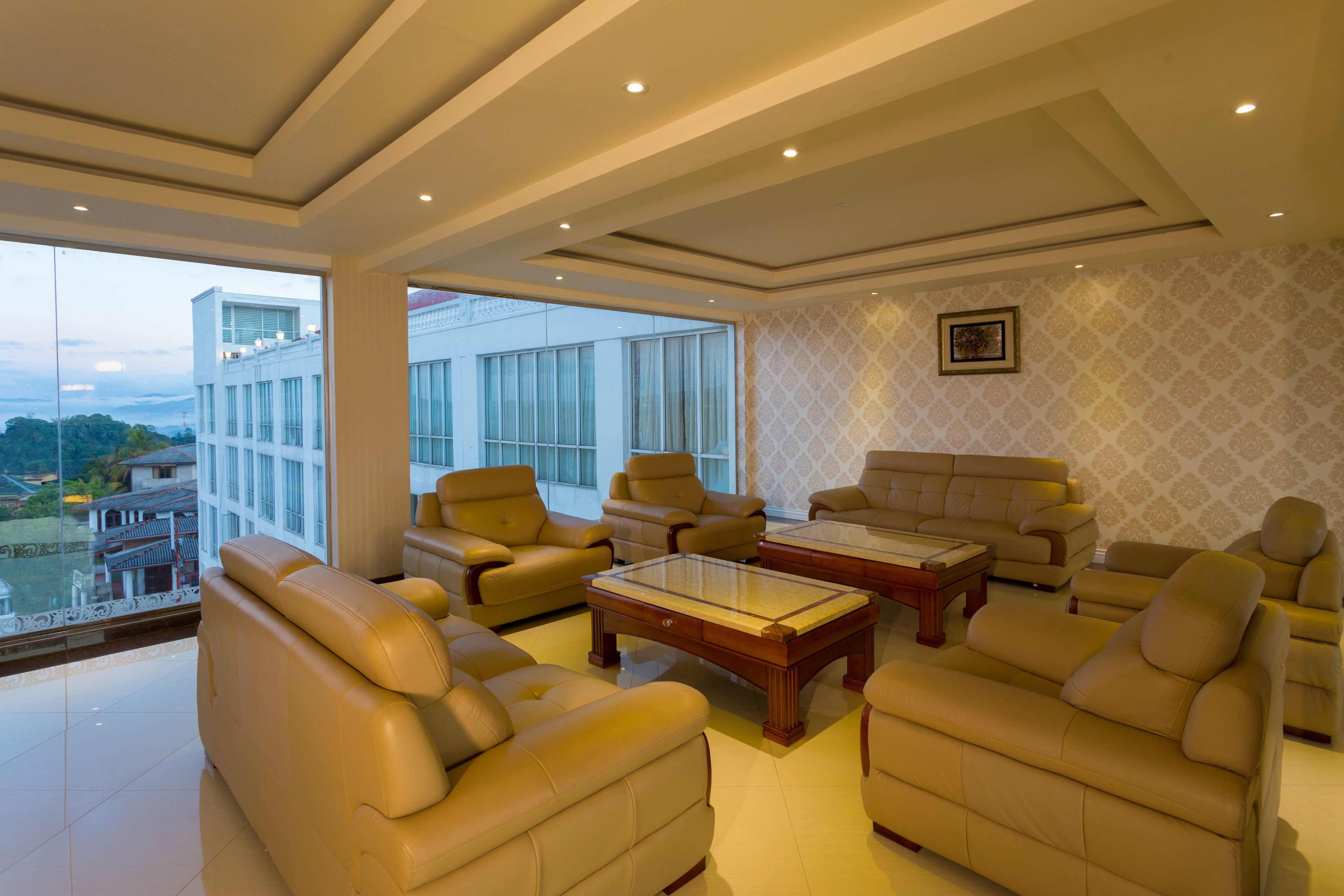 A spacious living room with leather sofas and armchairs, a wooden coffee table, and large windows offering a view of a modern building and greenery.