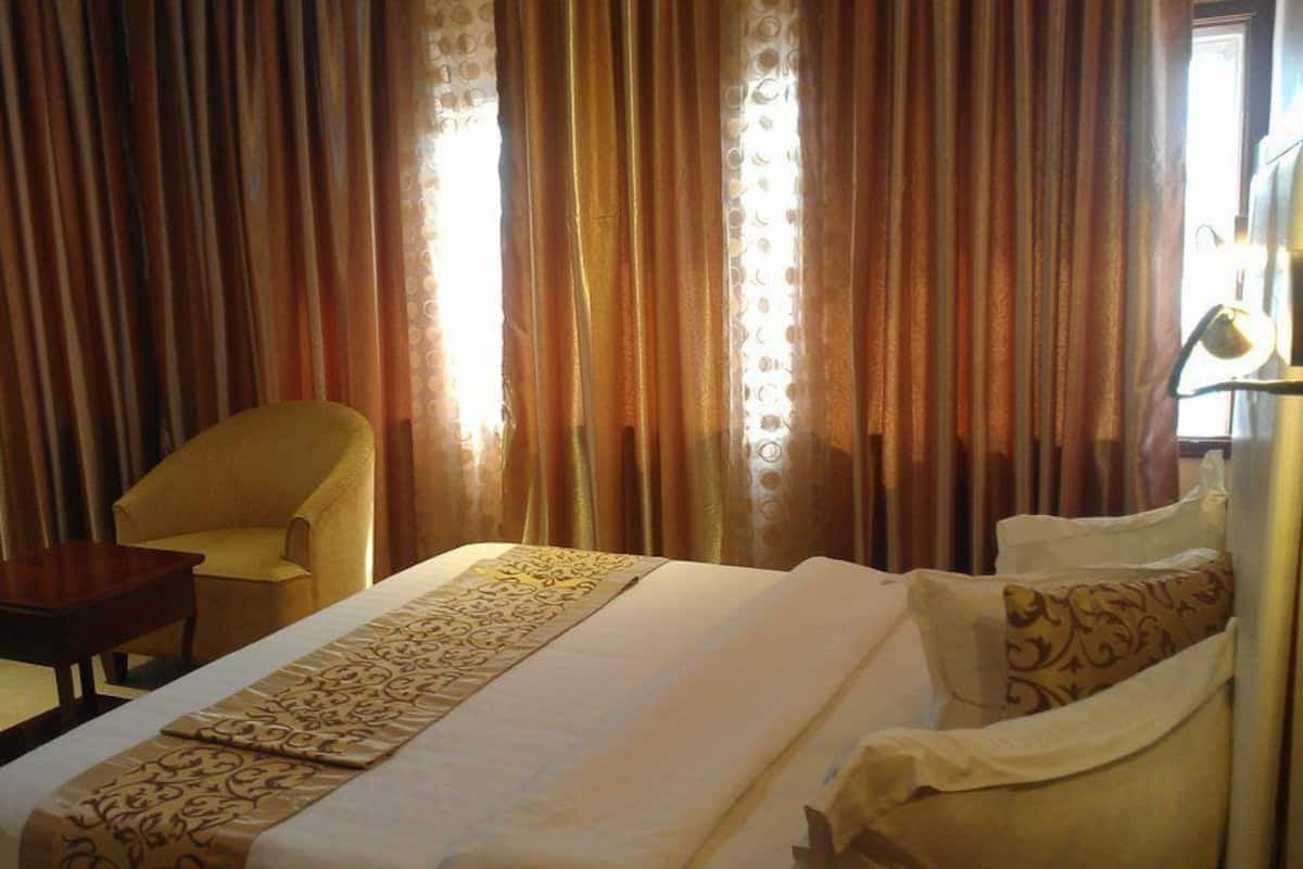 A hotel room with a bed, a chair, a small table, and curtains.